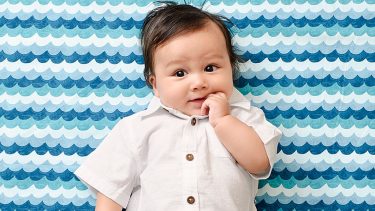 5个月大的婴儿穿着白色的纽扣，把一根手指放进嘴里