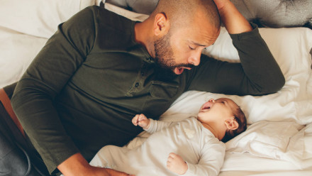 一个父亲对着床上的婴儿做鬼脸