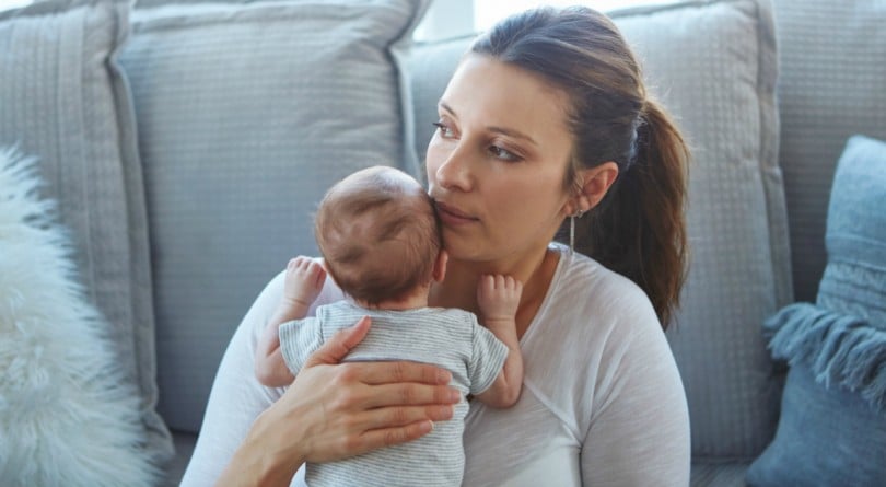 妈妈抱着孩子坐在沙发上，考虑着她是否应该放弃母乳喂养