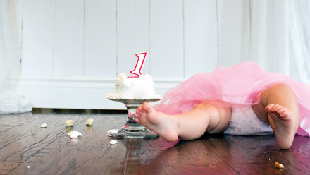 婴儿躺在地板上，手里拿着破碎的一岁生日蛋糕