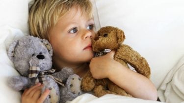 一个小男孩躺在床上抱着他的泰迪熊因为他感觉不舒服