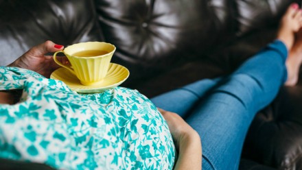 一个孕妇躺在沙发上，肚子上放着一杯茶