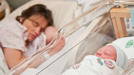 一位母亲睡在医院的病床上，旁边是她刚出生的孩子。