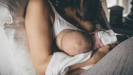 一个穿着哺乳胸罩的妇女在床上给她的婴儿喂奶