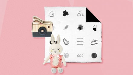 粉色背景与极简主义的婴儿玩具，如布兔子，婴儿垫和木制相机
