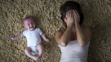 母亲和哭泣的婴儿坐在地毯上，母亲捂着脸