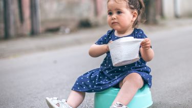一个蹒跚学步的女孩拿着手纸坐在街上的便盆上