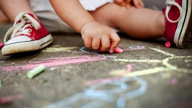 小孩(只看得见脚)在人行道上用粉笔画画