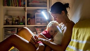 一位母亲在晚上开着灯给她蹒跚学步的孩子喂奶