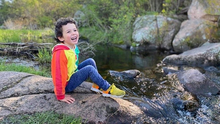 一个小男孩坐在瀑布旁对着镜头微笑