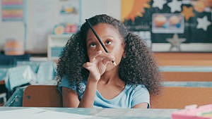 一个小女孩在课堂上努力集中注意力，却盯着她的铅笔