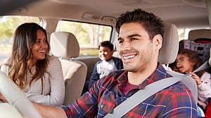 一个男人微笑着和他的妻子和家人一起开车