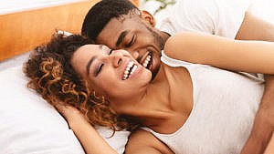 一对情侣在床上笑着拥抱的照片