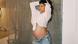 凯莉·詹娜站在一堵灰色的墙前。她把头发竖起来，露出怀孕的肚子。