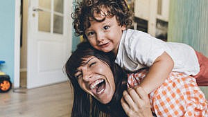 一位妈妈和爬在她背上的孩子玩耍，笑得很开心