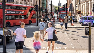 母亲和两个孩子穿过伦敦市中心一条繁忙的街道，背景是双层巴士