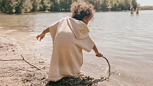 一个孩子穿着Kylo & Co中性沙滩罩衣在沙滩上玩耍。