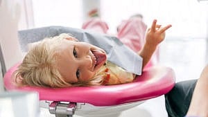 一个女孩在牙医办公室伸出舌头并做和平手势的照片。