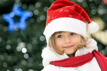一个穿着圣诞老人服装的小女孩在圣诞装饰品前微笑