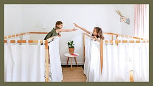 两个女孩在挂着窗帘的单人床上牵手
